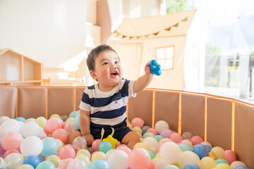自然光の室内でボールプールに入れられて楽しそうに遊ぶ0歳生後10か月の赤ちゃん