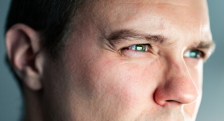Squinting eyes of a man looking at screen. Poor eyesight, bad vision. Light from laptop computer or phone. Guy watching tv. Focus on work. Closeup of face. Nearsightedness or myopia. Monitor reflect.