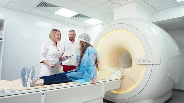 In a modern clinic, a female radiologist explains the good results of a CT scan of a young patient, observes and analyzes the CT scan next to a modern CT scanner.