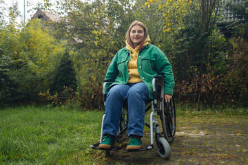 Fototapeta na wymiar Happy smiling cheerful Caucasian woman in stylish clothes on a wheelchair relaxing alone in autumn garden park