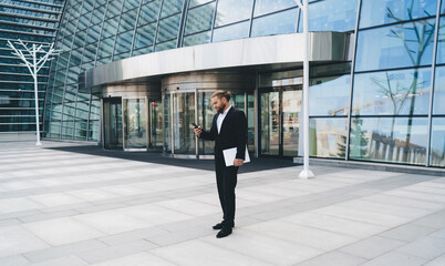 Busy businessman standing in front of modern building entrance