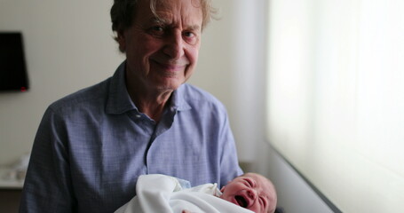 Grand-father smiling to camera while holding newborn baby
