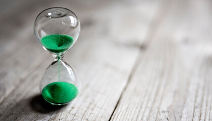 Hourglass with green sand time passing background concept for business deadline, urgency and running out of time - obrazy, fototapety, plakaty