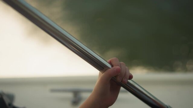 Child holds steel pipe by hand while rides motor boat under rainy cloud in summer closeup. Kid enjoys yacht sailing at seaside time lapse. Family vacation activity
