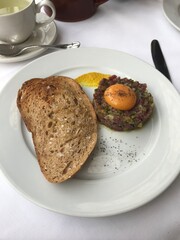 Close up of a plate of steak tartare and toast at a fancy white table cloth French restaurant