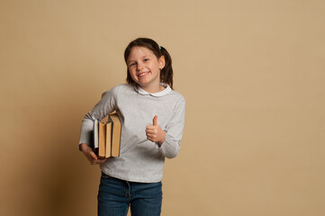 school girl smiles, hand up and holds big book. Concept back to school
