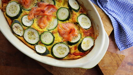 Zucchini gratin with salmon and parmesan on a wooden background. Summer pie with zucchini