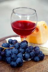 Composition with a glass of red wine, grapes and cheese. Red natural wine, cheese and a bunch of grapes in a garden in nature.