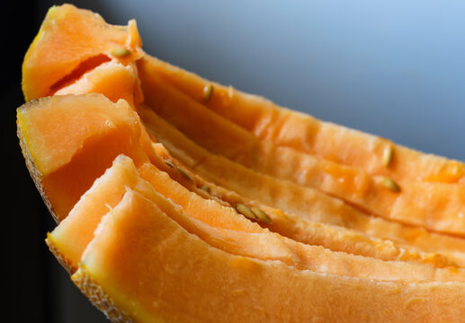 Roughly cut yellow slices of ripe melon, close-up, gray-white background