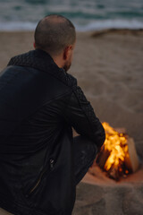 A man warms himself sitting near a fire at the beach