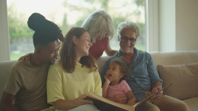young married multiethnic couple with daughter at grandparents home looking together to old family photo album
