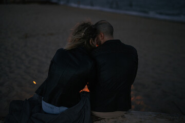 Back view couple sitting together near campfire on the beach