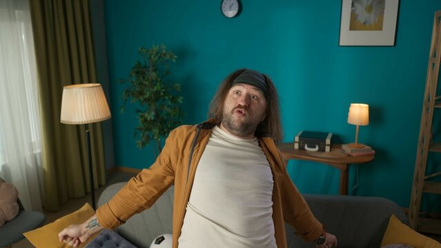 In the picture above a middle aged man stands. On the sofa there is a soccer ball. He looks to the side with his hands spread and something screams. Demonstrates the joy of a football teams butt