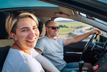 Fototapeta na wymiar Portrait of cheerful smiling young woman with husband have auto journey inside modern car. Safety riding car, car sharing and traveling concept image.