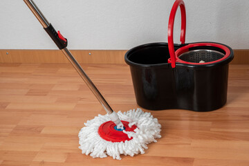 Cleaning concept mop and bucket. Cleaning products and spin mop with red details on the floor in an...
