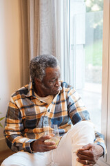 Retired senior man sitting on the floor by the window with sad face. Concept: lifestyle, abandonment, sad