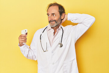 Doctor holding infrared thermometer in studio touching back of head, thinking and making a choice.