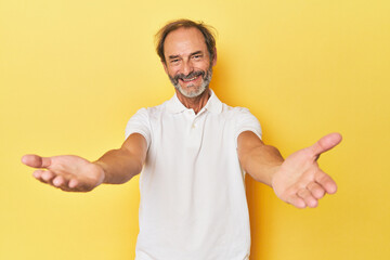 Caucasian middle-aged man in yellow studio showing a welcome expression.