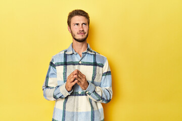 Fototapeta premium Young Caucasian man on a yellow studio background making up plan in mind, setting up an idea.