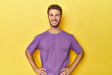 Young Caucasian man on a yellow studio background confident keeping hands on hips.