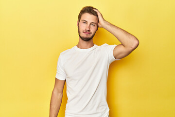 Young Caucasian man on a yellow studio background tired and very sleepy keeping hand on head.