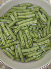 cleaning cut green beans with water, aka french or string beans or snaps, vegetable preparing for cooking in a bowl, taken straight from above in selective focus
