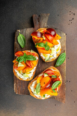 Gourmet sandwiches bread toast, bruschetta with cream cheese, peaches, tomatoes and green basil leaves on a wooden board. vertical image. top view. place for text