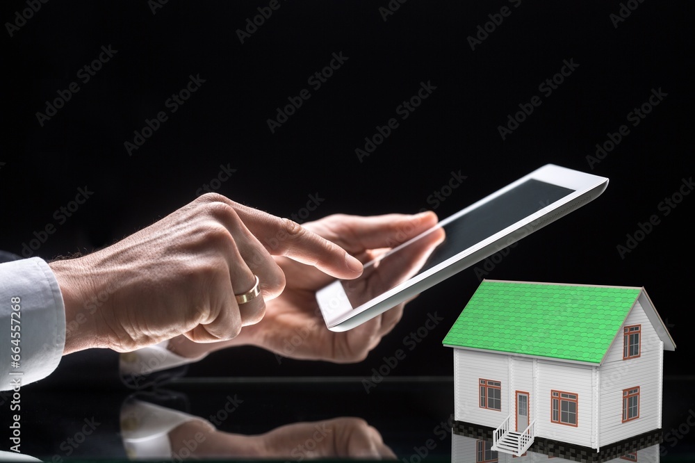 Poster Man holding digital tablet with house model on the desk