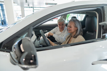 An elderly couple chooses a new car at a car dealership. Mature woman driving. 