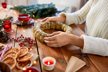 winter holidays, diy and hobby concept - close up of woman with decorations making christmas wreath at home