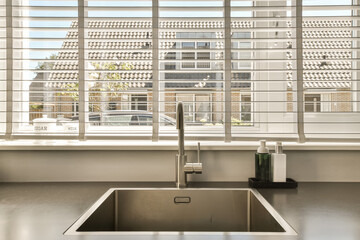 a kitchen sink in front of a window with shutters on the outside, and a view of a street