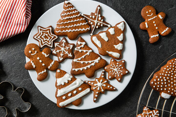 baking, cooking, christmas and food concept - close up of iced gingerbread cookies on plate, mold and kitchen towel on black table top
