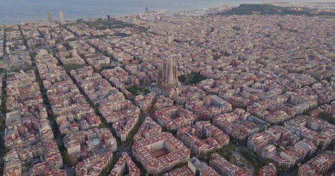 Cinematic aerial of Barcelona city skyline. Drone fly over Eixample residential famous urban grid and Sagrada Familia cathedral with morning sunrise cityscape. Catalonia, Spain. Travel Destination.