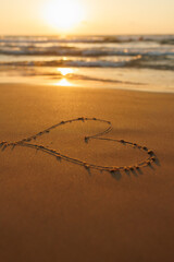 A heart is drawn on the sand on the beach at sunset. Romantic sunset on the beach. Heart shape. Heart symbol.
