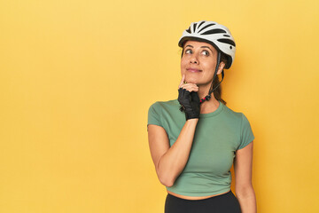 Cyclist middle aged woman with helmet and gloves posed looking sideways with doubtful and skeptical expression.