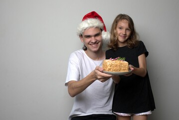 Portrait of children brother and sister with cake in their hands. Teen brother in Santa Claus hat