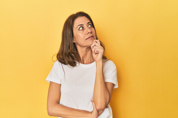 Middle-aged caucasian woman on yellow thinking and looking up, being reflective, contemplating, having a fantasy.