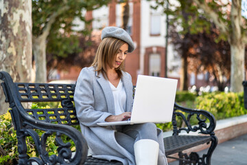 Young adult woman working with a laptop in a city park.