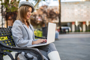 Mature beautiful business woman working on a laptop sitting on the bench in the street