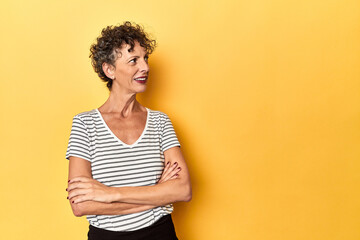 Mid-aged caucasian woman on vibrant yellow smiling confident with crossed arms.