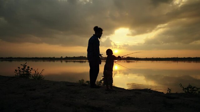 Fishermen are using fishing rods in the reservoir during Silhouette sunset, father teaching son how to fish in beautiful sunset over ocean ,activity family concept