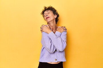 Mid-aged caucasian woman on vibrant yellow hugs, smiling carefree and happy.