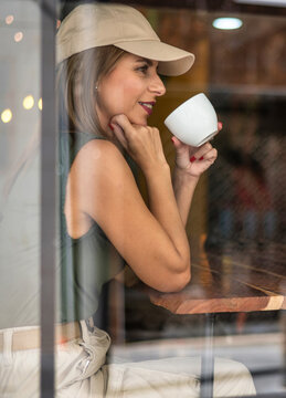 Alone and smiling woman inside a coffee shop. Young adult woman in a cafe photographed through window.