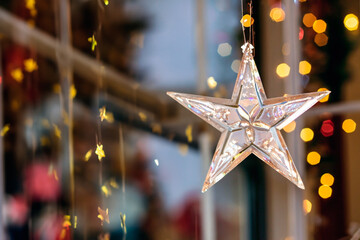 Glass Christmas star hanging from a window and Christmas lights in the background.