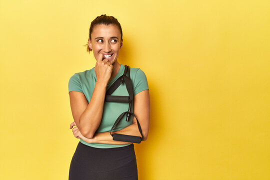 Middle aged sportswoman with resistance band on yellow relaxed thinking about something looking at a copy space.