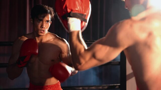 Asian and Caucasian Muay Thai boxer unleash punch in fierce boxing training session, delivering punching strike to sparring trainer, showcasing Muay Thai boxing technique and skill. Impetus