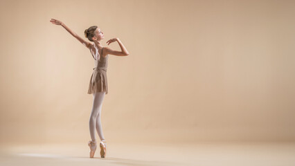 Beautiful young girl professional student ballerina in pointe shoes and a leotard on a light beige background.
