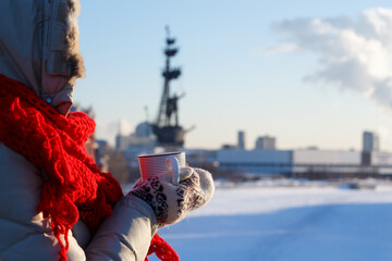 Woman in winter with a mug of hot drink on the background of a blurred image of the ice-covered Moscow river. Soft focus, close-up.