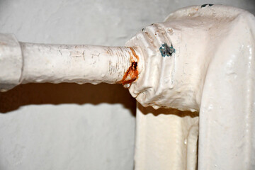 a rusted leaking pipe and an old cast-iron heating radiator with peeling white paint on the wall in...