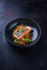Traditional Mediterranean salmon fish fillet with vegetable cuscus served as close-up on a design bowl with copy space